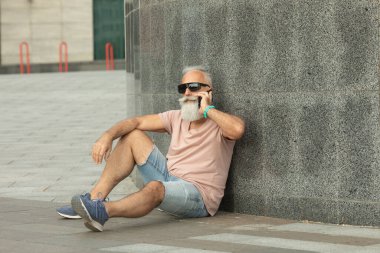 Hippi, güneş gözlüğü takan, akıllı telefondan konuşan, şehirde oturan olgun bir adam.