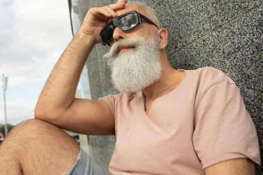 Hipster 'ı yakından gören olgun bir adam güneş gözlüğü takıyor ve şehrin ön cephesine yaslanıyor.