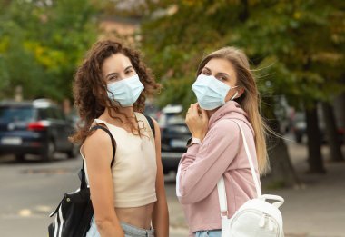 Coronavirus, Covid-19 tarafından korunmak için yüz maskesi takan iki genç arkadaş sokakta buluştu ve güvenlik mesafesinde kaldı..