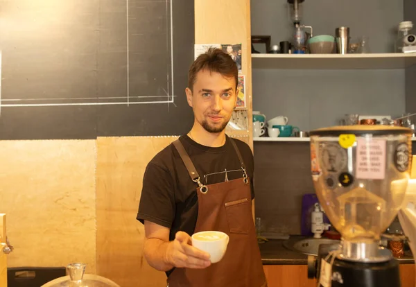 Knappe Barista Schort Met Een Kop Koffie Glimlachend Aan Bar — Stockfoto