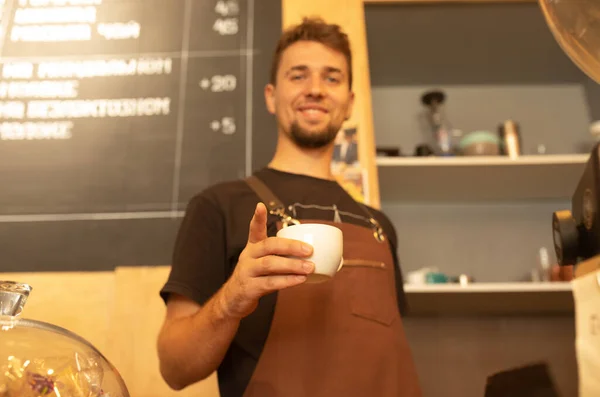 Knappe Barista Schort Met Een Kop Koffie Glimlachend Aan Bar — Stockfoto