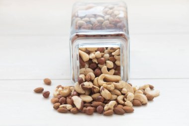 Fıstıklar cam kavanozdan beyaz ahşap arka plana saçılmış.