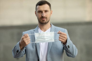 Covid-19 ya da Coronavirus konsepti: elinde tıbbi maske tutan yakışıklı bir esmer adamın portresi. Seçici odak.