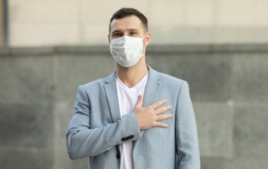 Cerrahi maske takan bir adam elini kalbinin üzerine koyarak selam veriyor. Coronavirus Covid-19 salgını nedeniyle Dünya Sağlık Örgütü tarafından önerilen yeni karşılama.