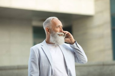 Beyaz saçlı, sakallı, ceketli, telefonda konuşan heyecanlı yaşlı adam..