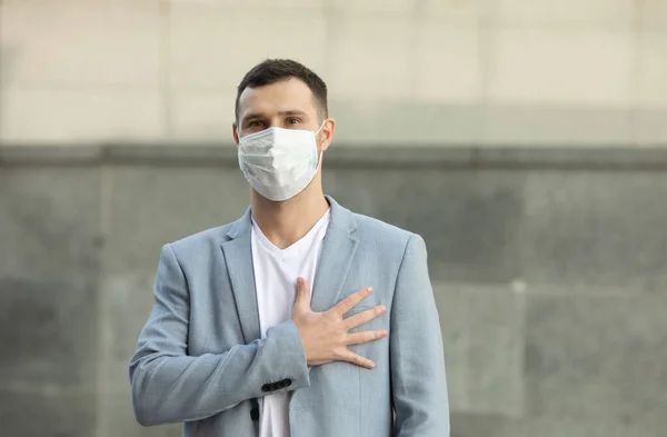 man wearing surgical mask greets with his hand over the heart. The new greeting recommended by the World Health Organisation due to the Coronavirus Covid-19 pandemic.