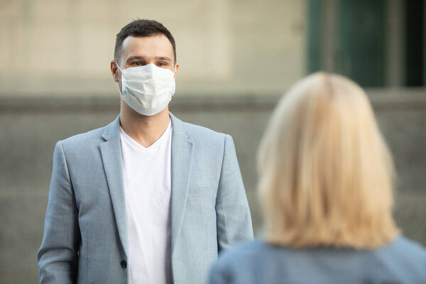 Мужчина и женщина в защитных масках, стоящих на расстоянии 2 м друг от друга, сохраняя социальную дистанцию, избегая распространения коронавируса. Ковид-19. 