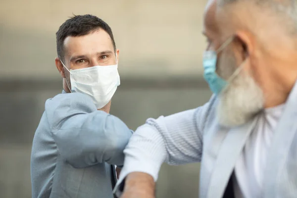 Two men wearing protective masks greeting in front of the wall - New normal handshake elbow bump to prevent contact and virus spread in covid-19 coronavirus pandemic - Social distancing concept.