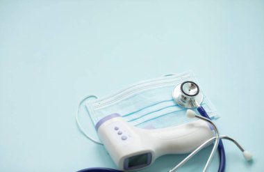 Sıcaklığı ölçmek için dijital tıbbi kızılötesi temassız termometre silahı, Coronavirus COVID-19 testi için mavi arka planda yüz maskesi. Tıp konsepti. Karantina salgını. Kendine dikkat et..
