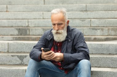 Dışarıdaki cep telefonunu kullanarak yaşlılara sakal bırakmış. Yeni moda akıllı telefon uygulamalarıyla eğlenen modaya uygun olgun bir adam..