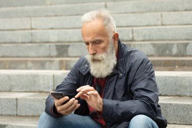 Dışarıdaki cep telefonunu kullanarak yaşlılara sakal bırakmış. Yeni moda akıllı telefon uygulamalarıyla eğlenen modaya uygun olgun bir adam..