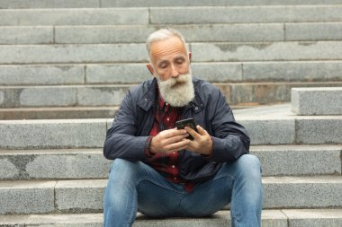 Dışarıdaki cep telefonunu kullanarak yaşlılara sakal bırakmış. Yeni moda akıllı telefon uygulamalarıyla eğlenen modaya uygun olgun bir adam..