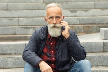 Dışarıdaki cep telefonunu kullanarak yaşlılara sakal bırakmış. Yeni moda akıllı telefon uygulamalarıyla eğlenen modaya uygun olgun bir adam..