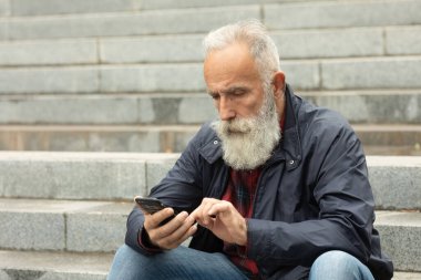 Dışarıdaki cep telefonunu kullanarak yaşlılara sakal bırakmış. Yeni moda akıllı telefon uygulamalarıyla eğlenen modaya uygun olgun bir adam..