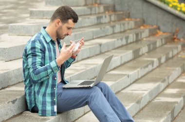 Adam dışarıda, merdivenlerde dizüstü bilgisayar üzerinde çalışırken koruyucu yüz maskesi takıyor..