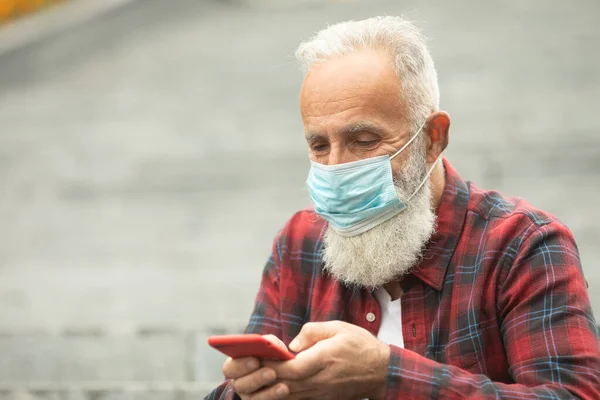 Bearded senior man with medical face mask using the phone to search for news. Stop the infection, man wear protective mask against infectious diseases and flu. Covid-19.