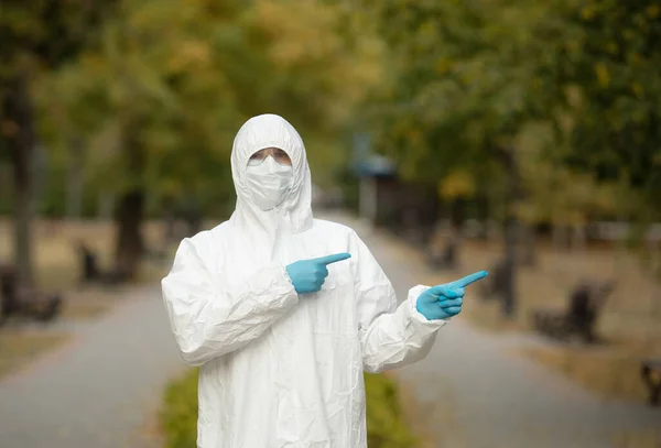 Doctor man in medical suit sterile face mask gloves on street . Epidemic pandemic coronavirus 2019-ncov sars covid-19 flu virus. Pointing finger aside up.