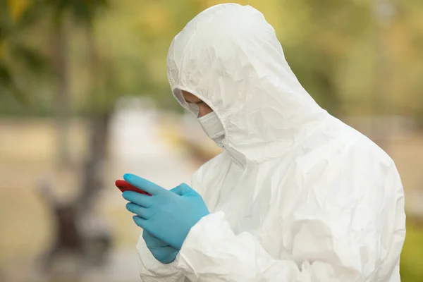 Man in a protective suit mask and gloves uses a smartphone for communication with family. Epidemic pandemic new rapidly spreading coronavirus 2019-ncov, medicine flu virus concept. Covid-19.