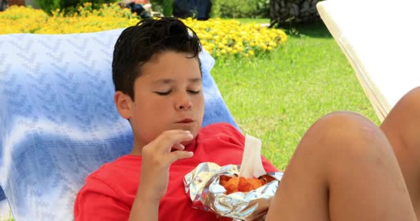 一个可爱的青春期小学生躺在日光浴和吃薯片的肖像 — 图库视频影像