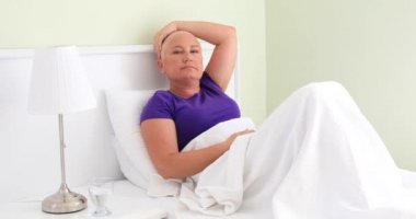 Kadın kanser hasta yatakta döşeme ve kameraya bakıyor