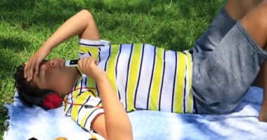 Bir çim döşeme ve parkta müzik dinlerken mutlu bir öğrenci portresi