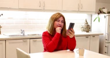 Orta yaşlı kadın mutfakta oturan ve evde cep telefonu konuşurken