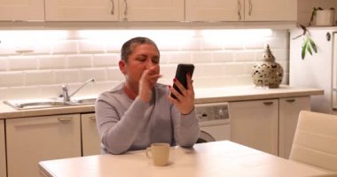 Mutfakta akıllı telefon kullanan kısa gri saçlı kadın.
