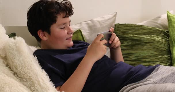 自宅でソファーに座っているスマートフォンで預け少年の肖像 子供は タイピング ゲームをプレイするために見ています インターネット通信と人の概念 スマートフォン中毒 — ストック動画