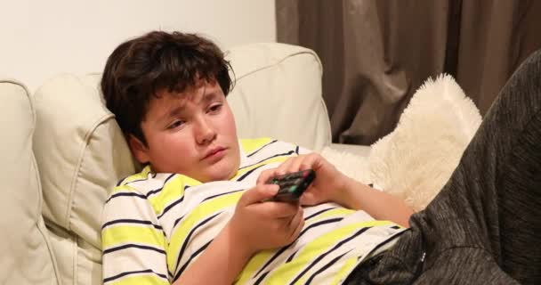 Уставший подросток лежит на диване и смотрит телевизор дома 2 — стоковое видео