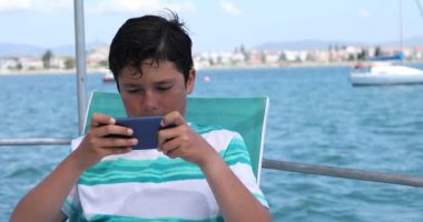 Teknede akıllı telefon kullanan genç bir çocuk.
