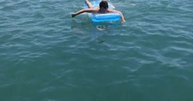 Delikanlı denizde yatakta yüzüyor.