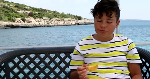 Jonge jongen eten aardappelchips op jacht dek in de zomertijd — Stockvideo