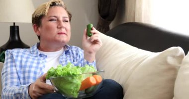 Taze diyet yemek yiyen ve evde televizyon izleyen bir kadının portresi.