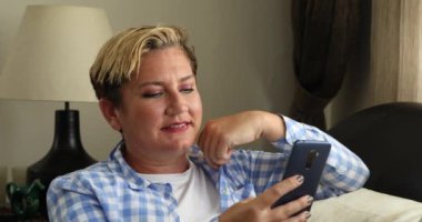 Kanepede oturan ve evde akıllı telefon kullanan bir kadın.