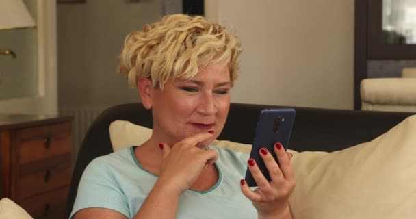 Μεσήλικη Γυναίκα Που Κάθεται Στον Καναπέ Και Χρησιμοποιεί Έξυπνο Τηλέφωνο — Αρχείο Βίντεο