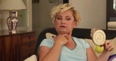 Diyet yapan orta yaşlı bir kadının portresi aynaya bakıyor ve diyetteki yeşil elma yiyen şişman boynuna üzülüyor.