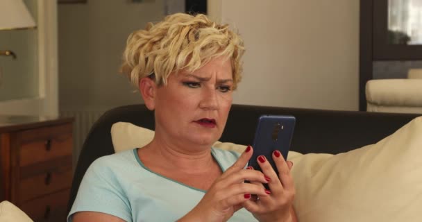 一个拿着智能手机的中年金发女人的画像震惊了 — 图库视频影像