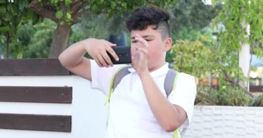 Dışarıda tek başına oturan yakışıklı bir gencin portresi. Çocuk ekranı seyrediyor, okuyor, daktilo ediyor, oyunlar oynuyor. Teknoloji, internet iletişimi ve insan konsepti, akıllı telefon bağımlılığı