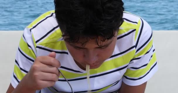 夏休みにボートデッキでパスタを食べるティーネージャーの肖像写真幸せな若い男の子はカメラを見て笑顔 — ストック動画