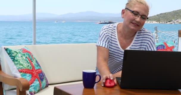中年のフリーランスの女性の肖像画は 夏休みにラップトップコンピュータとヨットのデッキに座っています — ストック動画