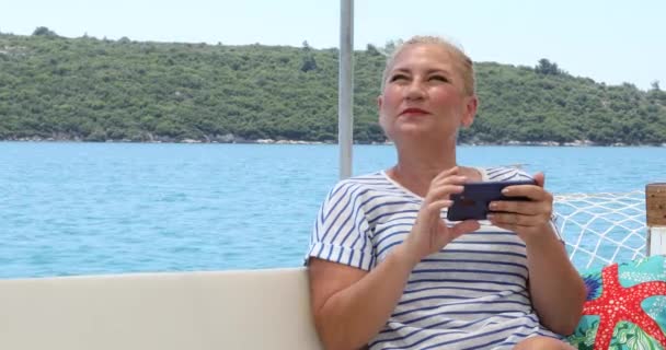 一个中年美丽的高加索女人的画像是在暑假时带着智能手机坐在游艇的甲板上 — 图库视频影像