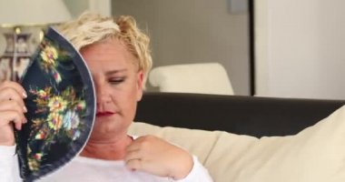 Orta yaşlı bir kadının portresi sıcak hava dalgasına maruz kalıyor. Evdeki oturma odasında bir kanepede oturuyor.