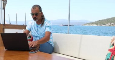 Yaz tatilinde bir yatın güvertesinde dizüstü bilgisayarlı orta yaşlı bir adamın portresi.