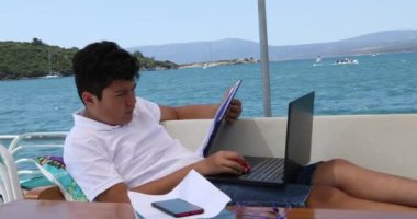 Yat güvertesinde okuyan genç çocuk, karantina ya da tecrit sırasında evde eğitim gören çocuklar için eğitim mesafesi öğreniyor.