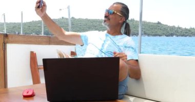 Yakışıklı, esmer adam lüks yat güvertesinde dinleniyor ve yaz tatilinde selfie çekiyor.
