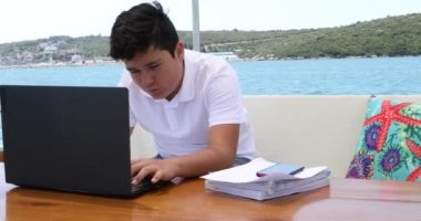 Yat güvertesinde okuyan genç çocuk, karantina ya da tecrit sırasında evde eğitim gören çocuklar için eğitim mesafesi öğreniyor.