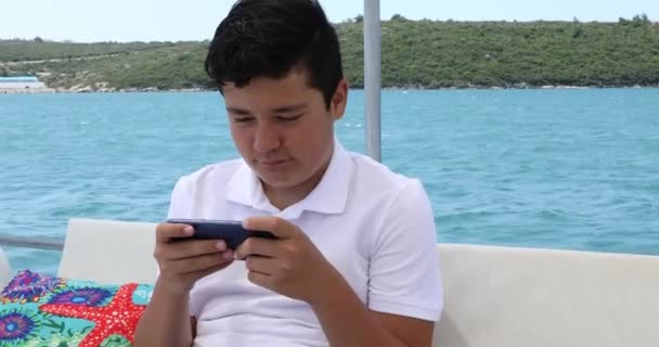 在阳光灿烂的夏日 一个高加索少年在游艇上用智能手机玩电子游戏的肖像 — 图库视频影像