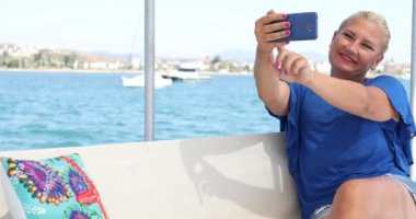 Beyaz tenli sarışın kadın yaz teknesi seyahati sırasında selfie çekiyor.