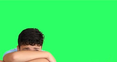 Kollarını yeşil ekran arkasına saklayan korkmuş genç bir çocuk.