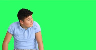 Yeşil arka planda kameraya başparmak gösteren genç bir çocuk.